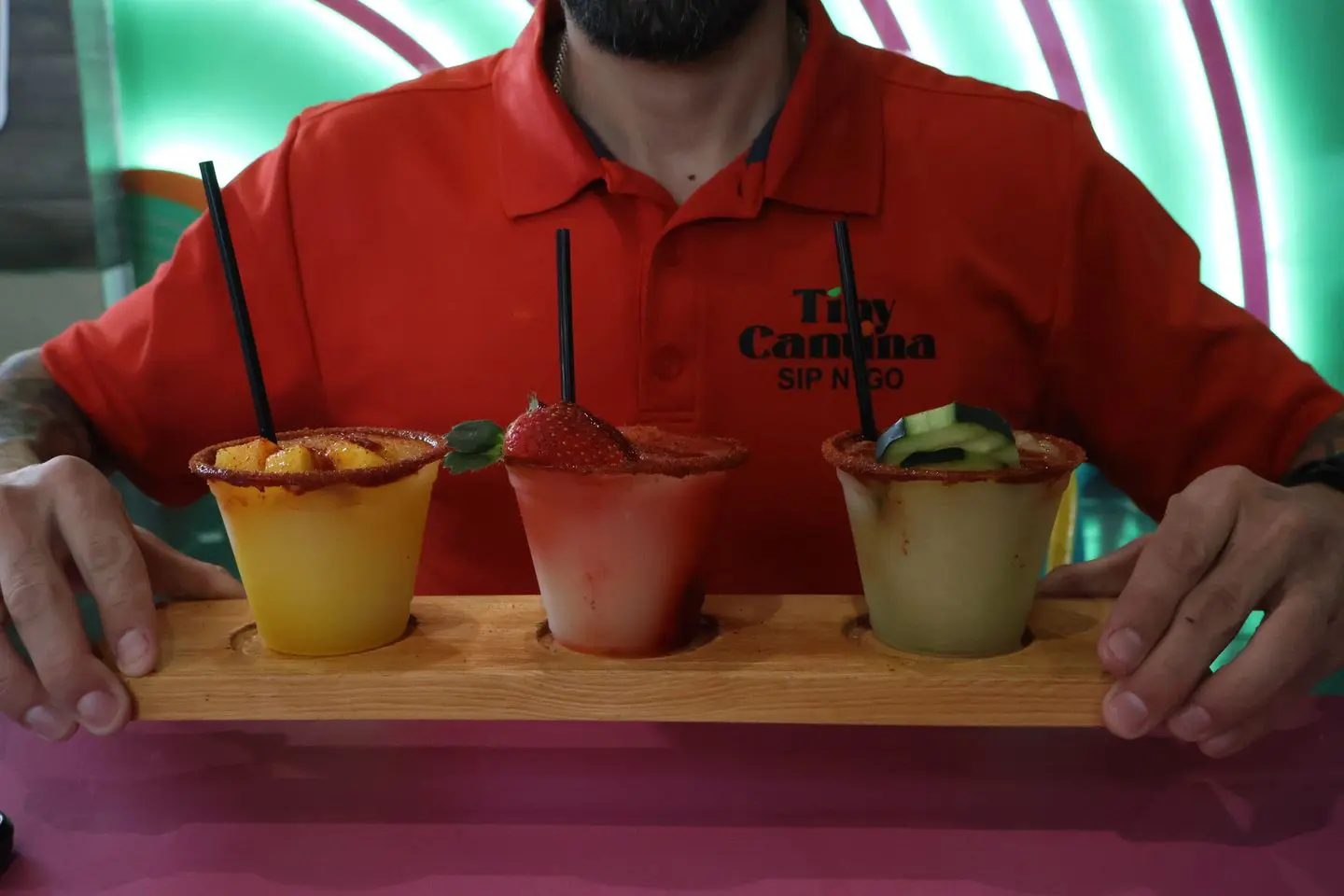 Three colorful cocktails served in small cups on a wooden tray.